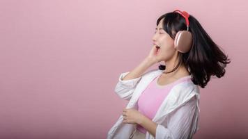 happy young asian woman model with stylish trendy sun glasses enjoy listening music by headphone audio and dancing isolated on pink studio background. technology, girl fashion, accessory concept. photo