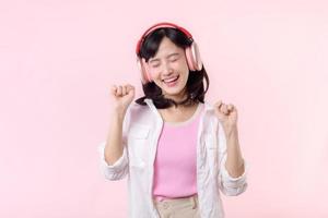Smile pretty asian model person listen music song and enjoy dance with wireless headphone online audio radio sound. Positive fun exited joyful youth female woman on pink isolated background studio photo