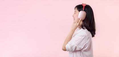 Side view young smiling cheerful fun woman she wear pink shirt white t-shirt headphones listen to music use mobile cell phone isolated on plain pastel light pink background. People lifestyle concept. photo