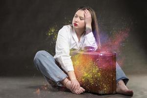 Beautiful girl sits with a vintage suitcase on a gray background. photo