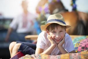 A funny little boy in a straw hat lies on a cart looking at the camera and smiles. photo