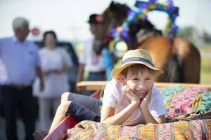 A funny little boy in a straw hat lies on a cart looking at the camera and smiles. photo