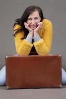 Happy fifty year old woman in yellow clothes with vintage suitcase on gray background. Portrait of a middle-aged woman. photo