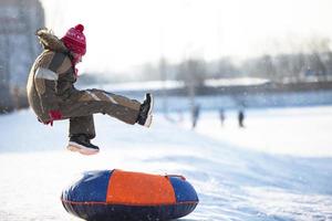 Little child on a sleigh. Child on a winter day. A boy is riding on a snow slide. photo