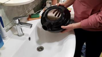 een vrouw giet vuil water van een vacuüm schoonmaakster tank na schoonmaak. de werkwijze van schoonmaak de tapijt met een vacuüm schoonmaakster met een water filter. video