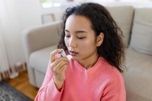 Asian woman using inhaler while suffering from asthma at home. Young woman using asthma inhaler. Close-up of a young Asian woman using asthma inhaler at home. photo