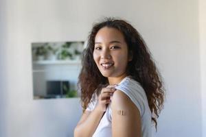 mujer señalando a su brazo con un vendaje después recepción el covid-19 vacuna. asiático mujer demostración su hombro después consiguiendo coronavirus vacuna foto