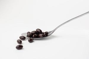 Black soft gel capsules in a stainless steel spoon on a white background. Vitamin food supplements photo