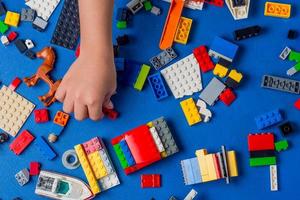 niño manos jugando y edificio con vistoso el plastico ladrillos en un azul mesa. temprano aprendizaje y motor desarrollo de niños a un temprano edad, el concepto de educativo construcción foto