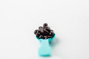 Black soft gel capsules in a blue spoon on a white background. Vitamin food supplements photo