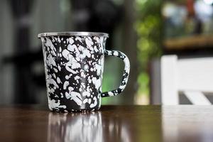 Black and white patterned old metal mug or enamel cup on a wooden table on blur background photo