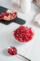 Grains of a ripe pomegranate in a bowl and in a spoon and a part of a pomegranate on a light table. Organic natural food. Vertical view. Close-up photo