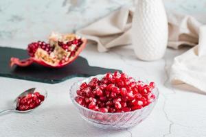 Grains of a ripe pomegranate in a bowl and in a spoon and a part of a pomegranate on a light table. Organic natural food. Lifestyle photo