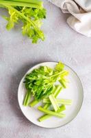 Sliced fresh celery stalk with leaves on a plate on the table ready to eat. Vegetarian food. Vertical and top view photo