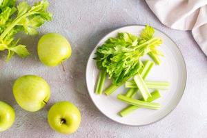 Sliced fresh celery stalk with leaves on a plate and green apples on the table ready to be cooked. Vegetarian food. Top view photo