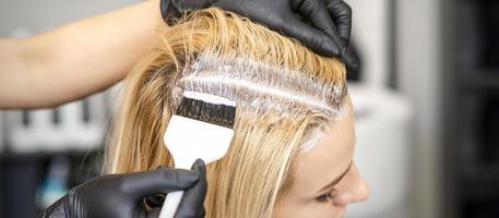 Hairdresser dyeing blonde hair roots photo