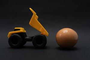 un foto después algunos ediciones, un amarillo camión intentos a llevar un huevo, en negro antecedentes papel.