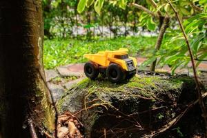 A photo after some edits. A yellow dump truck on a mossy stone.