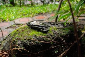 un foto después algunos ediciones un negro juguete coche en un cubierto de musgo Roca. un concepto de Vamos a naturaleza con clásico coche.