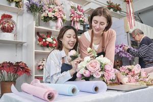 dos jóvenes y hermosas socias de floristería arreglando y decorando un montón de flores juntas sonríen con un trabajo feliz en una colorida tienda de flores con flores frescas, pequeña empresaria. foto