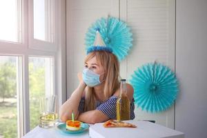 A sad man celebrates a birthday alone in a medical mask and looks boredly out the window. photo