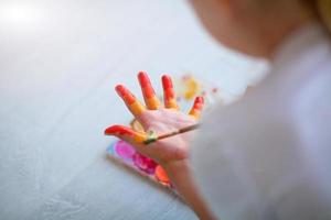 Child girl sitting on the floor and paints the palm of his hand. Quarantine. photo