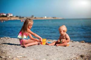 niños jugar en el playa. verano agua divertido para el familia. chico y niña con juguete cubos y un pala en el costa. foto