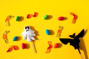 Top view of Halloween candy ghost, paper bat, jelly worms  on yellow background . photo