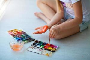 Child girl sitting on the floor and paints the palm of his hand. Quarantine. photo