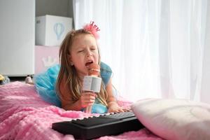 Beautiful little girl in a princess costume sings into a karaoke microphone. photo