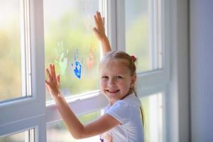 niños niña dibujar con palmas en el ventana. pintado manos salir un marca en el vaso. cuarentena. permanecer hogar. destello multitud sociedad comunidad en autoaislamiento cuarentena pandemia coronavirus. foto