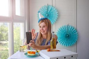 A woman in a sits in front of a smartphone and waves hello. photo