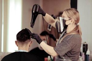 Hairdresser with security measures for Covid-19, blow-dry a man in a medicine mask, social distance, cutting hair with a medical mask, face shield and rubber gloves in a beauty salon photo