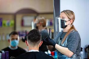 Hairdresser with security measures for Covid-19, cuts a man  social distance, cutting hair with a medical mask, face shield and rubber gloves. photo