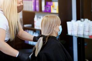 un cliente en un médico máscara se sienta en un Barbero. cuarentena período en ciudad es encima. pequeño negocio y COVID-19, coronavirus. mujer consiguiendo un nuevo Corte de pelo. foto