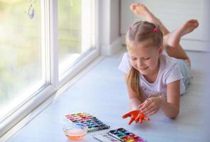 Child girl lies on the floor and paints a palm with paints. photo