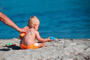 The male hand applies sunscreen to the baby is back. photo