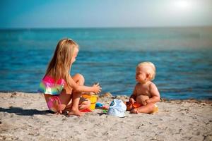 Children play on the beach. Summer water fun for the family. Boy and girl with toy buckets and a shovel on the seashore. Relax in the ocean with a baby and toddler. photo