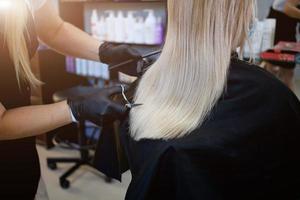 peluquero con seguridad medidas para COVID-19, un mujer en un médico mascarilla, social distancia, corte pelo con un médico máscara y caucho guantes en un belleza salón. foto