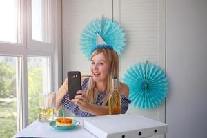 niña sentado en frente de el teléfono y comiendo pizza, selfie foto. en línea en cuarentena cumpleaños foto