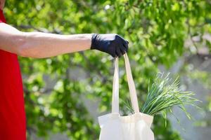 Male hand in rubber gloves holds out a grocery bag, outdoor. Fast and free Delivery transport . photo