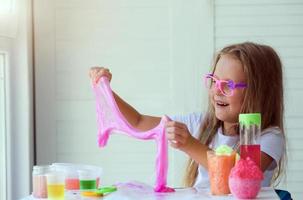 Little girl stretching pink slime to the sides. Kids hands playing slime toy. photo