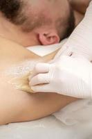 Beautician waxing young male armpit photo