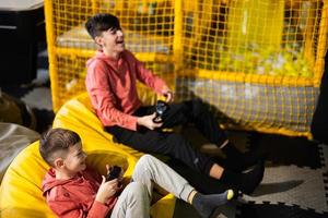 dos hermanos jugando vídeo juego consola, sentado en amarillo puff en niños jugar centro. foto