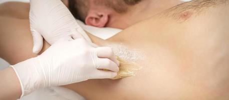 Beautician waxing young male armpit photo