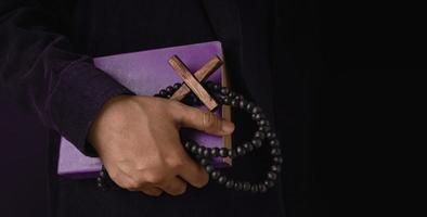 Spirituality, Religion and Hope Concept. Person Holding a Holy Bible, Bead and Cross. Symbol of Humility, Supplication, Believe and Faith for Christian People. Dark Tone, Close-Up and Side View photo