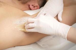 Beautician waxing young male armpit photo