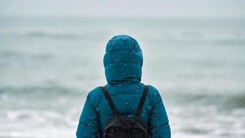 Girl in down jacket standing on seashore in winter photo