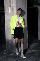 an asian man in a lime colored jacket leaning against a disused building pillar looking very handsome photo