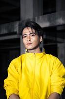 an Asian man with sleek black hair wearing a yellow jacket and jeans while posing photo